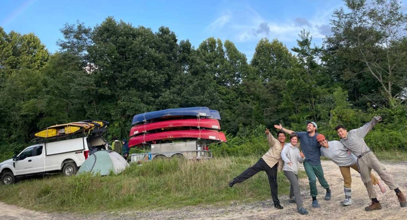 Five people pose for a photo in front of a truck pulling canoes. 